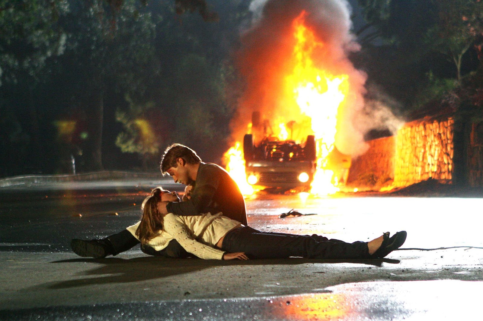 De fondo se ve un auto volcado incendiándose. Marissa está acostada en el suelo dando sus últimos suspiros. Ryan la recuesta entre sus piernas y la acaricia.