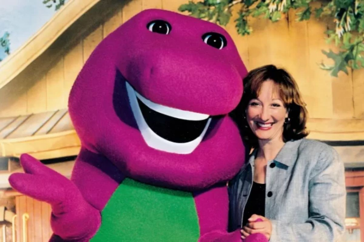 Barney el dinosaurio junto a Sheryl Leach, su creadora. Ambos sonrién a la cámara.