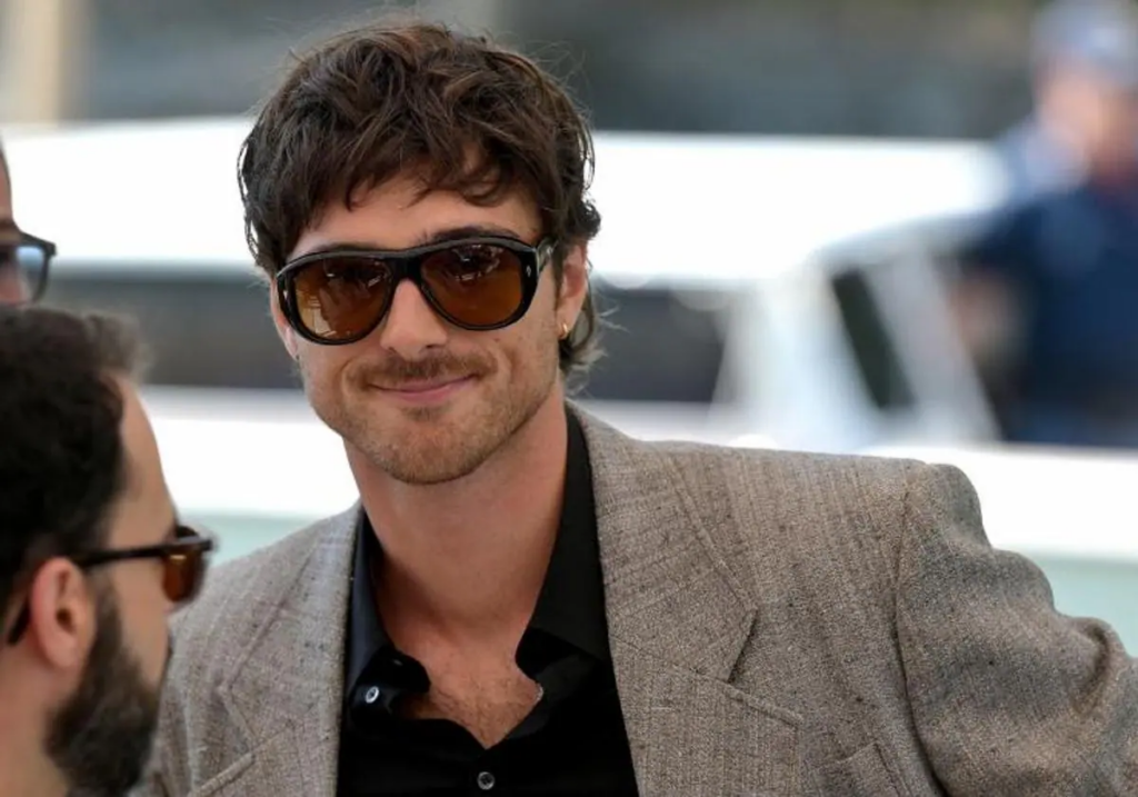 Jacob Elordi, con unos lentes grandes vestido formal y sonriendo en un primer plano. 