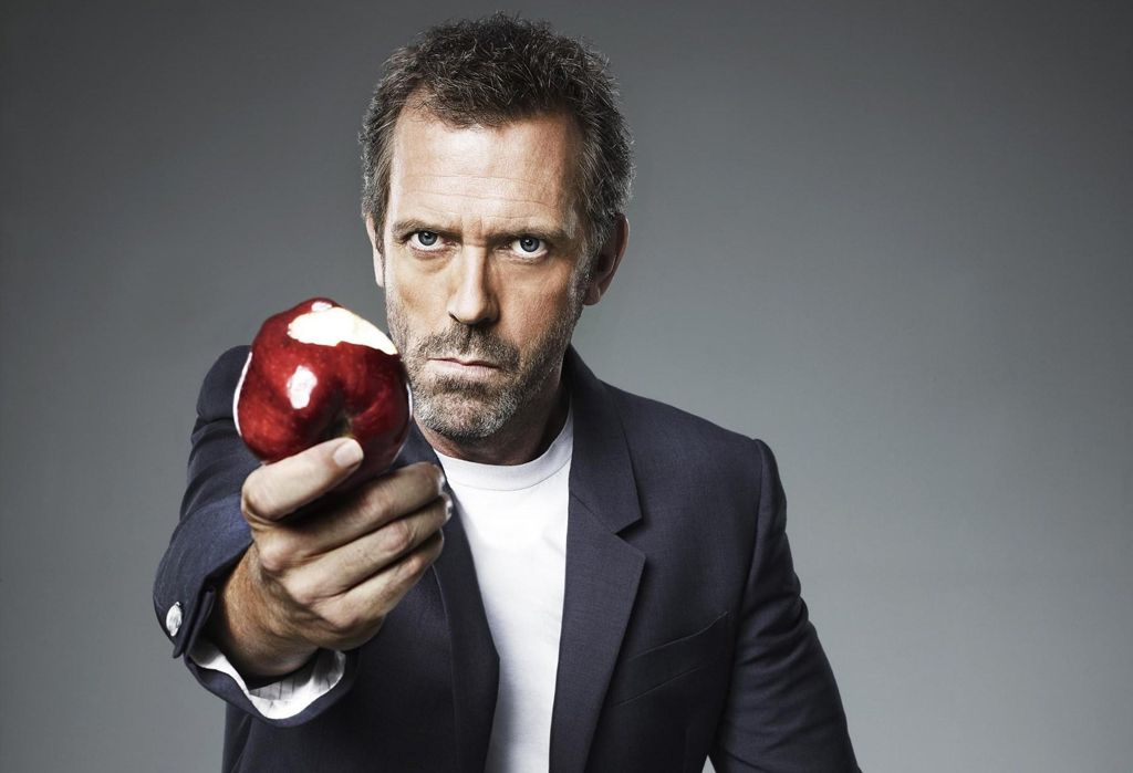 Dr. House (Hugh Laurie) extendiendo una manzana roja.
