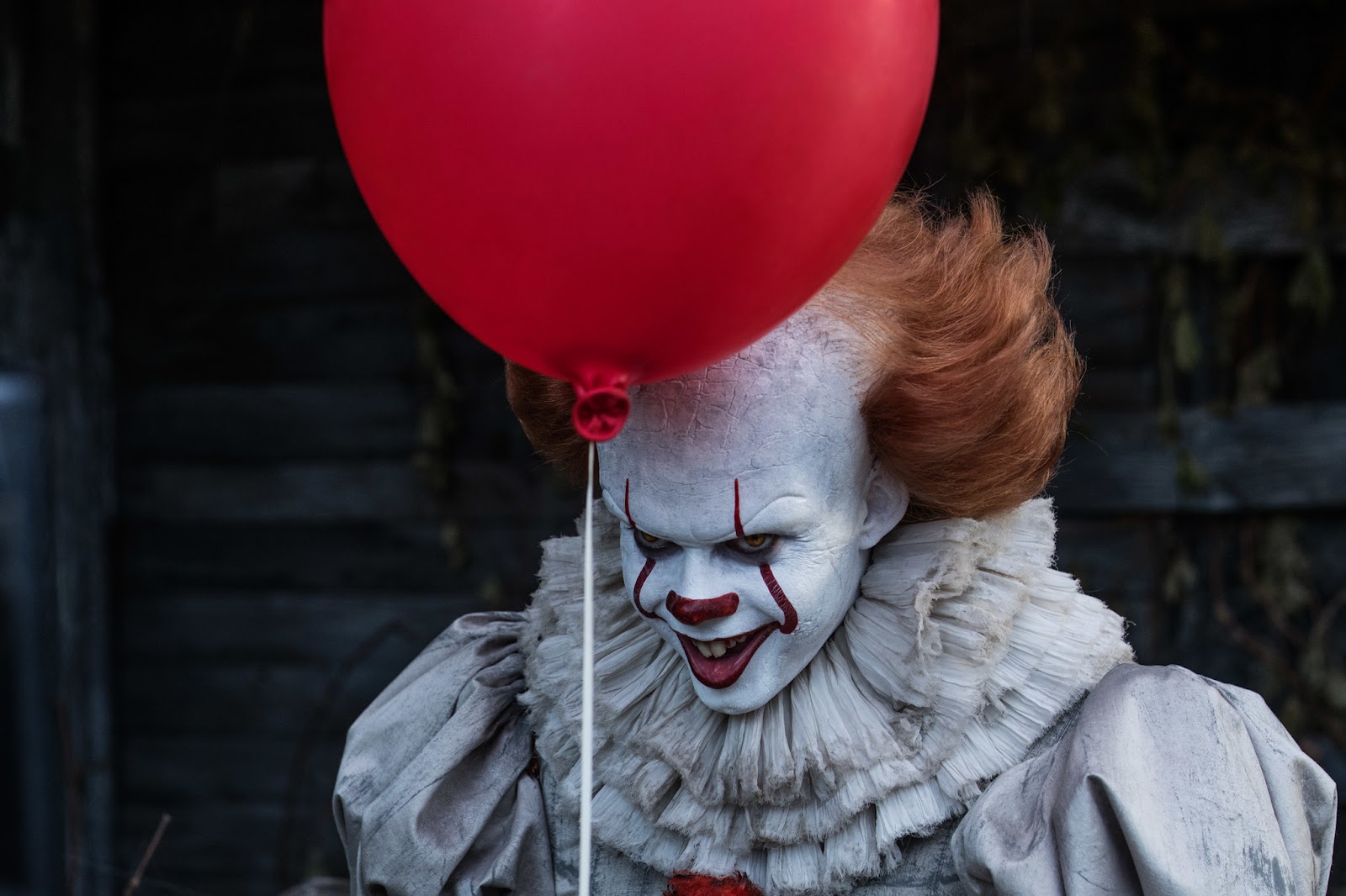 Pennywise con su traje blanco y sonrisa malévola, sosteniendo un globo rojo