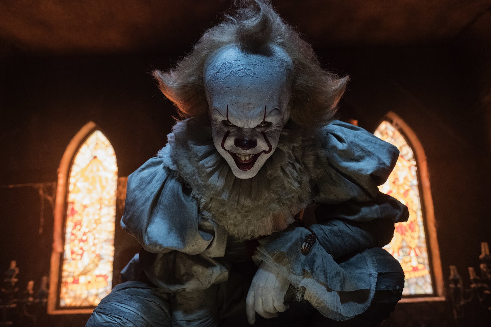 El payaso Pennywise en It, con su traje blanco y sonrisa aterradora, observando a la cámara