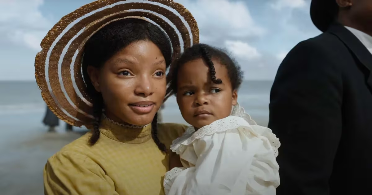 Halle Bailey en El color púrpura, portando un traje o vestido amarillo, un sombrero y con un bebé en brazos